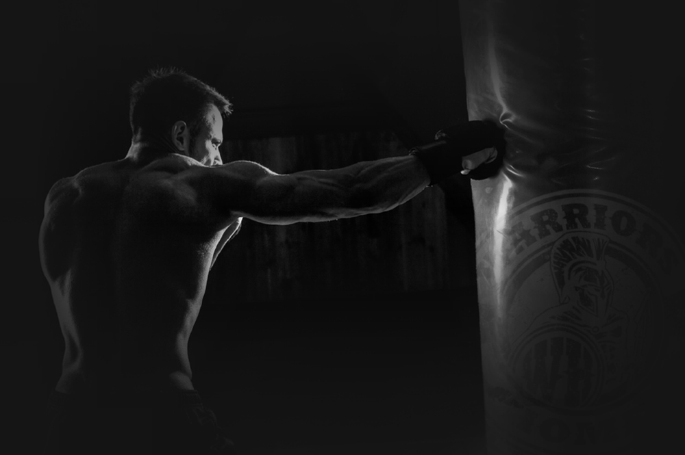 Young male boxer hitting punching bag on black background.